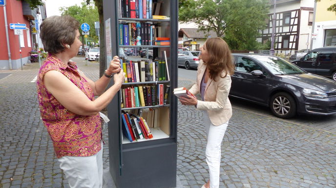 Ein Buchgeschenk zur Eröffnung: Bürgermeisterin Monika Böttcher (rechts) komplettiert die Buchsammlung, die Bücherschrank-Patin Brigitte Sauer betreut.