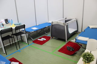 Blick in eine der Wohnkabinen, eingerichtet mit Feldbetten, Tisch und Stühlen sowie Hygieneartikeln.