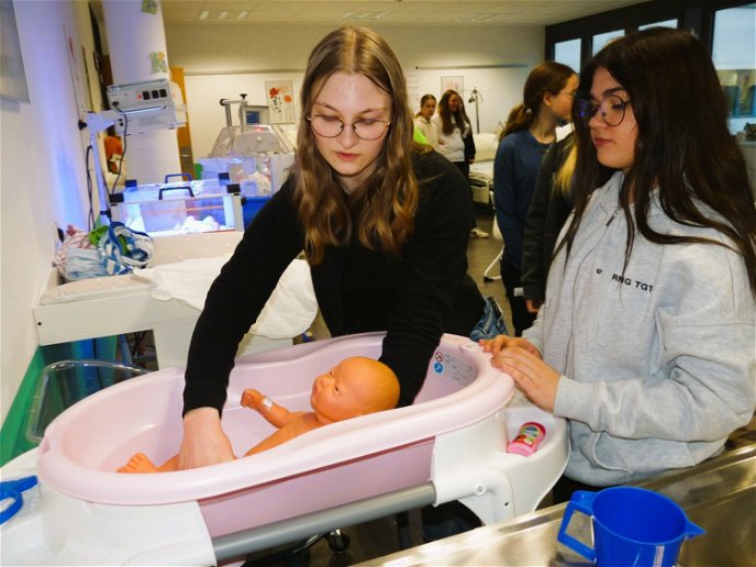 Auszubildende Anna-Sophie Lanz hilft einer Schülerin dabei,  ein Baby zu baden.