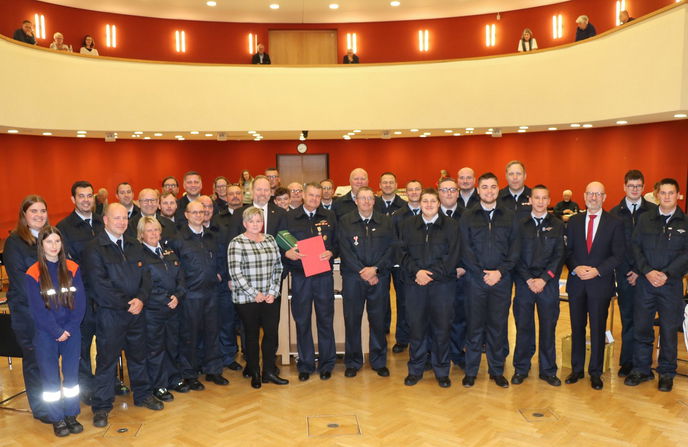 Die Kameraden mit Stadtbrandinspektor Kai Heger (hinter dem Geehrten in dritter Reihe) flankieren Frank Weigelt (Mitte) mit seiner Frau Carola (ohne Uniform) und Sohn Lukas (hinter dem Geehrten in zweiter Reihe).