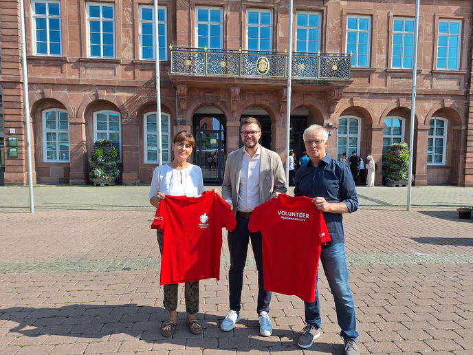 Antje Bach (Volunteerin), Bürgermeister Dr. Maximilian Bieri und Thomas Bach (Volunteer) präsentieren die Shirts, die alle ehrenamtliche Helfer der Special Olympics erhalten. 